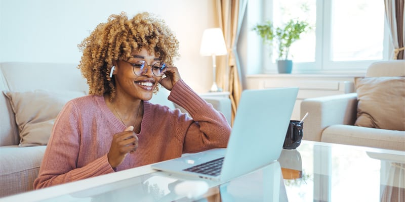 A smiling Black woman works on her laptop from home.