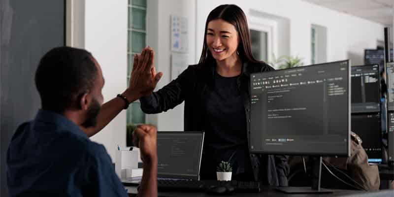 A woman high-fives a software developer at their desk.