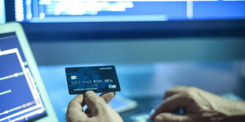 A image of a person holding a credit card in front of a computer.