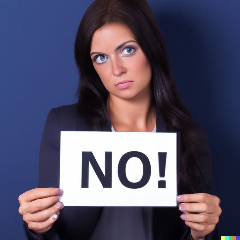 A woman wearing a business suit stares into the camera holding a sign that says "No!"